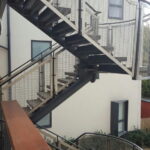 External steel staircase with curved landings and mesh style railings.